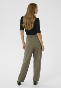 Pantalons larges vert olive à taille haute, dotés de poches arrière et d'une texture lisse. Associés à un haut noir ajusté.