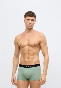 Męskie bokserki w jasnym zielonym materiale z czarnym elastycznym pasem w talii. Na pasie znajduje się logo. Gładka faktura i dopasowany krój.