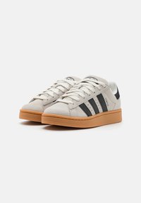Zapatillas de ante gris claro con rayas negras, diseño de cordones y suela de goma. Presentan un logo bordado y acentos cosidos.