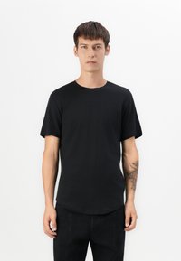 Camiseta de algodón negra con cuello redondo y mangas cortas; cuenta con un dobladillo ligeramente curvado y un diseño ajustado.