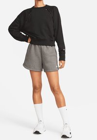 Sudadera negra con detalles recortados, combinada con pantalones cortos grises. Calcetines blancos y zapatillas deportivas completan el conjunto. Diseño simple y deportivo.