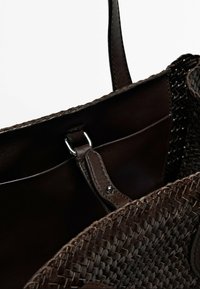 Geweven bruine tas met een glad leren interieur, zilveren hardware-accenten en een stevige handgreep, die een gestructureerd, gedetailleerd ontwerp toont.