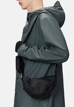 Persona che indossa un impermeabile grigio con cappuccio e guanti neri, mentre porta una borsa a tracolla nera con due scomparti con cerniera.