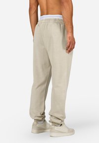 Šviesiai rudos sportinės kelnės su laisvu siluetu, elastingu juosmeniu ir apykaklėmis, pagamintos iš minkštos medžiagos. Dėvimos su šviesiomis sportinėmis bateliais.