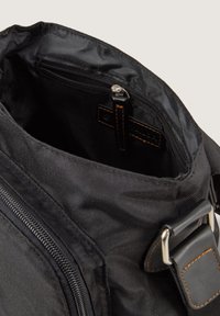 Borsa in tessuto nero con chiusura a zip, dotata di una tasca interna con zip e di una tracolla in pelle con hardware metallico e cuciture decorative.
