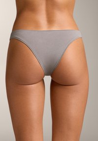 Siva bombažna tangica z gladko teksturo, minimalnim pokrivanjem in tankimi stranskimi trakovi, ki kaže brezšivno zasnovo in subtilne šivarske podrobnosti.