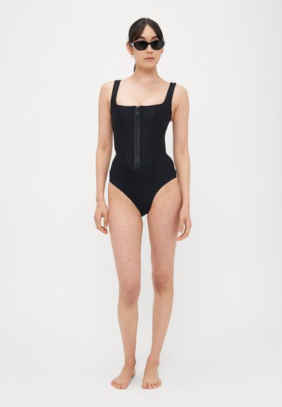 Černé jednodílné plavky s přiléhavým živůtkem a předním zipem. Mají široké ramenní popruhy a vysoký střih nohavic pro prodlouženou siluetu.