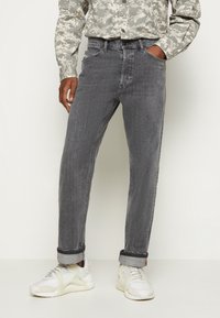 Gray denim jeans with a straight-leg fit, featuring five pockets, subtle stitching, and cuffed hems, paired with white sneakers.