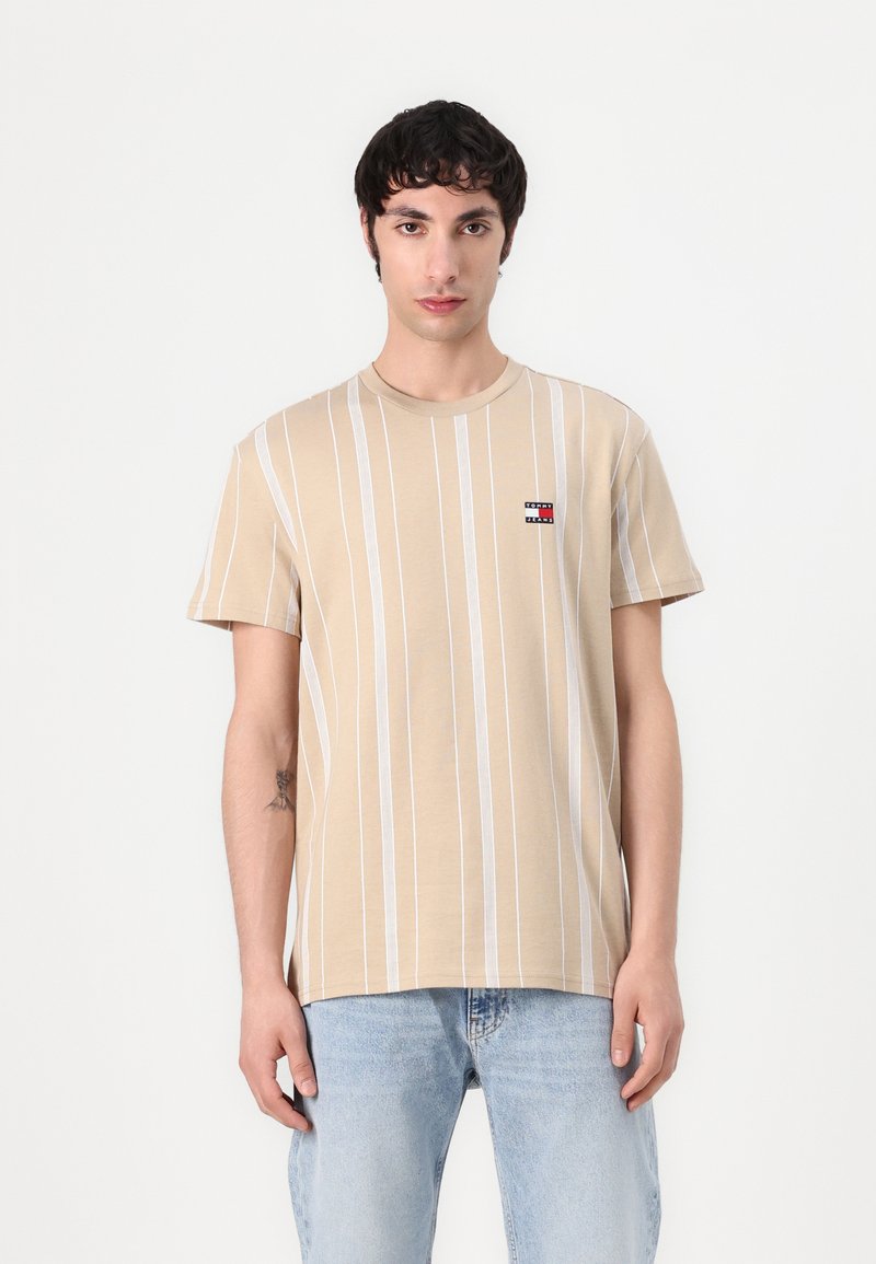 Beige short-sleeve T-shirt with vertical white stripes and a small embroidered logo on the left chest. Cotton material, round neckline, relaxed fit.