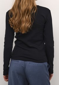 Top a maniche lunghe nero a coste abbinato a pantaloni blu navy a righe sottili. Focus sulla vista posteriore che mostra la texture del tessuto e i dettagli delle cuciture.