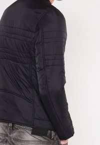 Schwarze Steppjacke mit horizontaler Naht, ausgestattet mit einem hohen Kragen und einem schlanken Design. Weiche, glatte Textur mit Reißverschluss-Taschen.