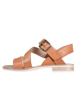 Tan leather sandal with crisscross straps, adjustable buckle, and a low stacked heel. Smooth texture with a subtle sheen and white sole.