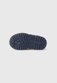 Semelle de chaussure en caoutchouc marine avec un motif texturé, présentant des rainures profondes et des accents circulaires pour l'adhérence. Zone de talon renforcée.