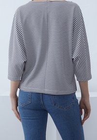 Randig topp med svart och vit horisontell rand, lös passform, 3/4-långa ärmar och rundad nederkant. Bärs med blå denimjeans.