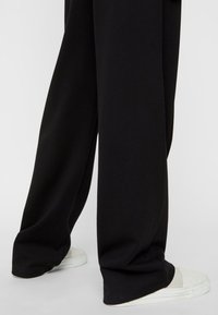 Black wide-leg trousers with a smooth texture and relaxed fit, featuring a high waist and white sneakers with a simple design.