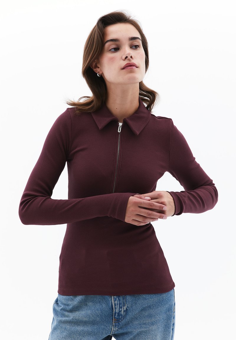 Burgundy pitkähihainen polo-paita vetoketjulla, ribbaakoostumuksella ja klassisella kauluksella. Yhdistetty rentoihin vaaleansinisiin farkkuihin.