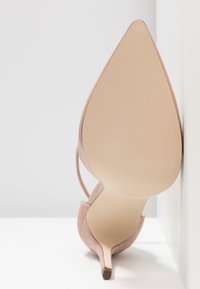 Zapato de tacón alto con un diseño de punta afilada. Hecho de un material rosa suave, presenta un respaldo texturizado y un tacón stiletto delgado.