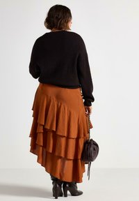 Sort, struktureret sweater over en orange lagdelt nederdel. Nederdelen har flæser og et svævende design, parret med sort knæhøjde støvler.