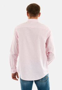 Camisa de manga larga rosa claro con cuello puntiagudo, puños con botón y dobladillo curvado, hecha de una tela texturizada y transpirable.