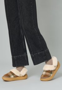 Pantofole slip-on a righe con colletto in pelliccia sintetica, colori marrone e beige, suola in gomma e dettagli beige. Indossate con pantaloni larghi scuri.