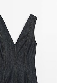 Robe sans manches en denim foncé avec un col en V profond et des détails de coutures verticales visibles sur un fond blanc.