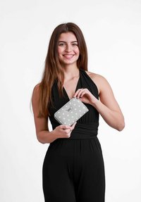 Šedá peněženka s bílými puntíky, se zipovým uzávěrem a embosovaným logem. Držena osobou v černém oblečení na jednobarevném pozadí.