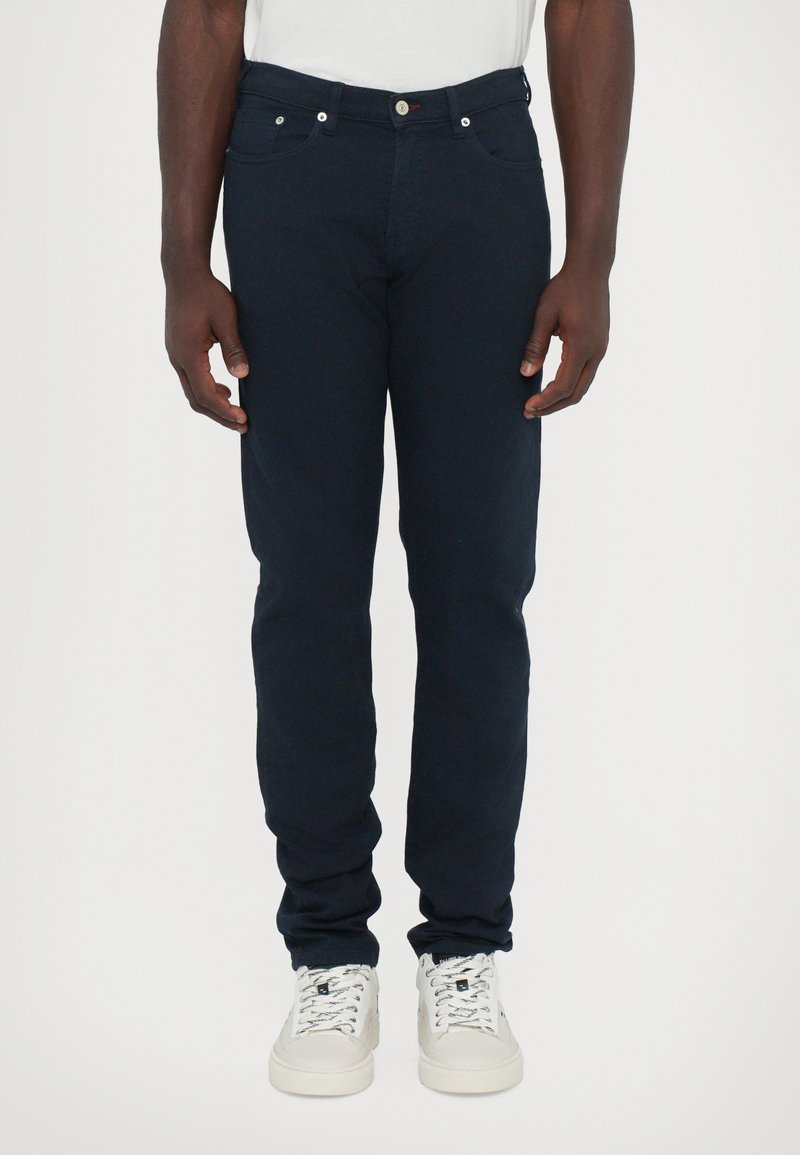 Jeans de mezclilla azul marino con corte ajustado. Las características incluyen un diseño de cinco bolsillos, cierre con cremallera, botones remachados y una textura suave.