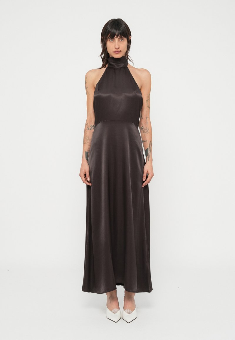 Barna szatén maxiruha pántos nyakkivágással, testhezálló felső résszel és lengő szoknyával. Simaságot és elegáns sziluettet kínál.