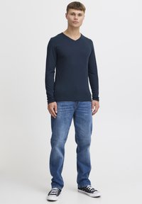 Marineblaues Langarm-V-Ausschnitt-Shirt, kombiniert mit klassischen blauen Jeans und schwarzen Leinenschuhen, mit einem lässigen Schnitt und glatter Textur.