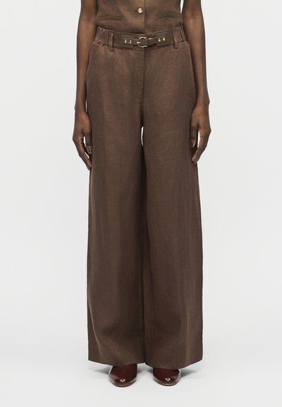 Pantalon marron à jambes larges et taille haute avec une ceinture assortie, porté avec des chaussures marron foncé sur une personne debout.