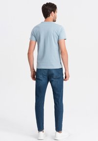 Lys blå bomulds T-shirt med korte ærmer og rund hals, parret med mørkeblå jeans, båret med hvide sneakers, set fra ryggen.