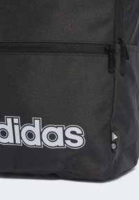 Zaino in tessuto nero con un grande logo bianco "adidas", due tasche con zipper e una piccola etichetta di branding in basso a destra.