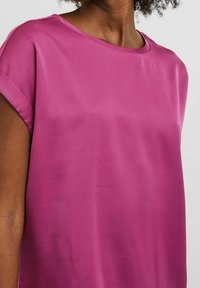 Top magenta a maniche corte con scollatura rotonda, texture liscia e vestibilità comoda. Il tessuto sembra leggero e traspirante.