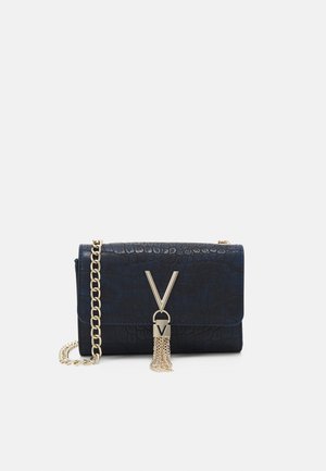 Pochette bleu marine à texture crocodile avec bandoulière chaîne dorée et fermoir doré en forme de V avec un pompon doré décoratif.