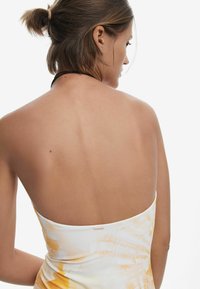 Robe bodycon avec un imprimé abstrait blanc et jaune, présentant un design sans bretelles, un tissu lisse et un accent de marque subtil à l'arrière.