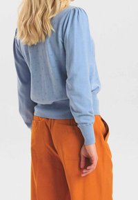 Ljust blå stickad tröja med puffiga axlar, med små dekorativa hål. Matchas med orange byxor med hög midja.