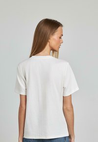 Camiseta de algodón blanca con un corte relajado, mangas cortas y cuello redondo; textura suave con costuras mínimas.