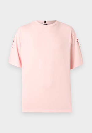 Lyserød oversized T-shirt med korte ærmer og rød tekst på begge ærmer, ensfarvet front og rund hals.