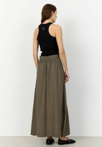 Top nero abbinato a una gonna maxi verde oliva, con una cintura elastica e spacchi laterali, indossato con scarpe basse nere.