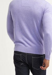 Lila ronde hals trui gemaakt van zachte stof, voorzien van een geribbelde zoom en boorden, gedragen met donkerdenim jeans.
