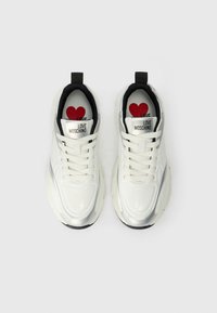 Sapatilhas brancas com textura brilhante e suave; detalhes em prata; interior preto; apresenta o rótulo "LOVE MOSCHINO"; palmilha com gráfico de um coração vermelho.