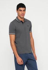Szara koszulka polo z czarnym kołnierzykiem, z białymi paskami na rękawach. Logo wyszyte na piersi. Dopasowany krój.