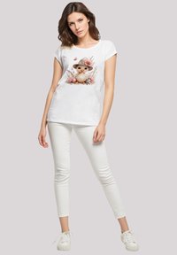 White cotton t-shirt featuring a cute animal print with floral accents. Paired with white skinny pants and white sneakers. Simple design.