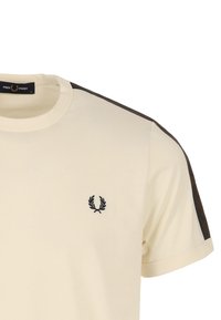 Kortärmelig crèmekleurige t-shirt met een zwart geborduurd embleem op de borst, voorzien van contrasterende donkere zijstrepen en een ronde hals.