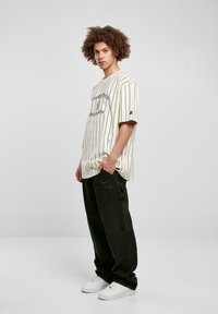Stribet creme t-shirt med sorte linjer og grafisk print i midten, parret med løse sorte cargo-bukser og hvide sneakers.