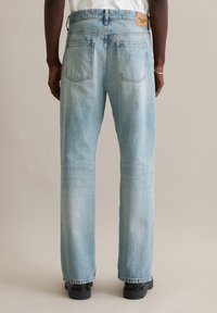 Jeans in denim azzurro chiaro con vestibilità comoda, caratterizzati da due tasche posteriori e da un'etichetta del marchio in pelle marrone sulla cintura. Tessuto testurizzato.