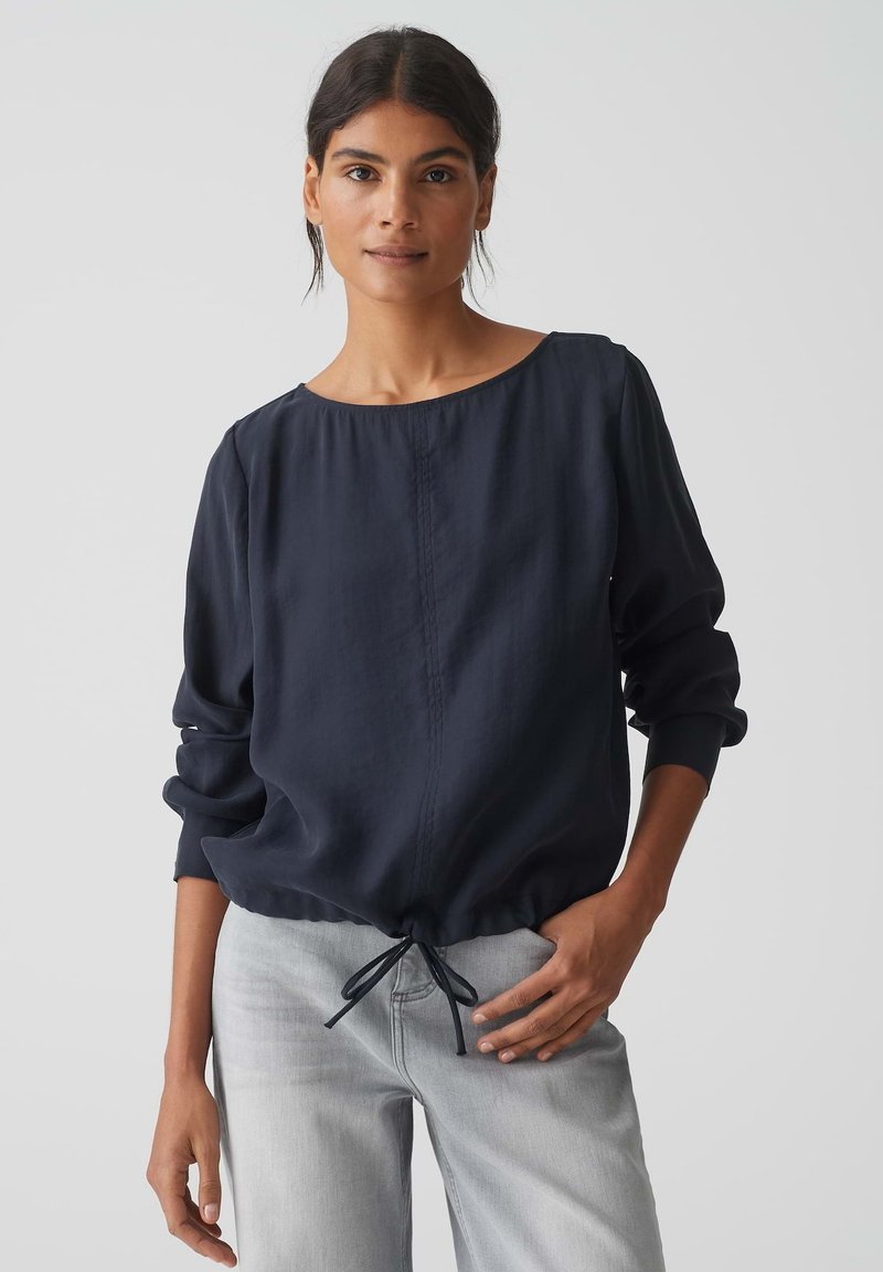 Blusa leggera di colore blu navy con un collo rotondo, polsini arricciati e orlo con cordoncino. Tessuto liscio con cuciture sottili. Vestibilità casual.