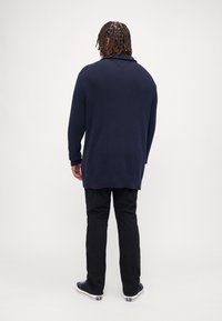 Granatowy sweter z prążkowanej dzianiny o głębokim kołnierzu, z długimi rękawami i luźnym krojem, połączony z czarnymi spodniami oraz niebiesko-białymi trampkami.