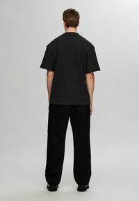 Svart, ribbad t-shirt med korta ärmar och rund halsringning, kombinerad med löst sittande svarta byxor. Enkelt design, inga synliga mönster eller accenter.