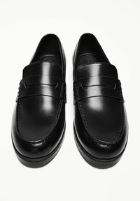 Black leather loafers with a smooth finish, rounded toe, and a decorative strap across the upper. Features subtle stitching details.